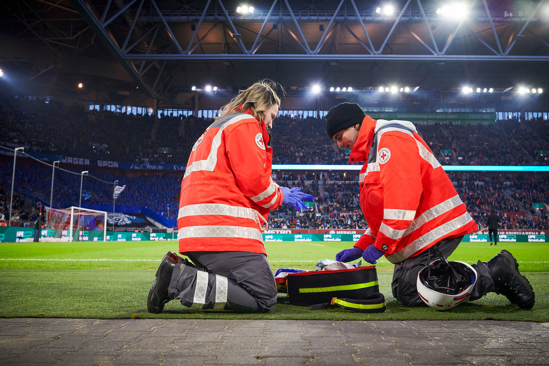 Zwei Sanitäter des DRK knien auf einem Fußbfallfeld.